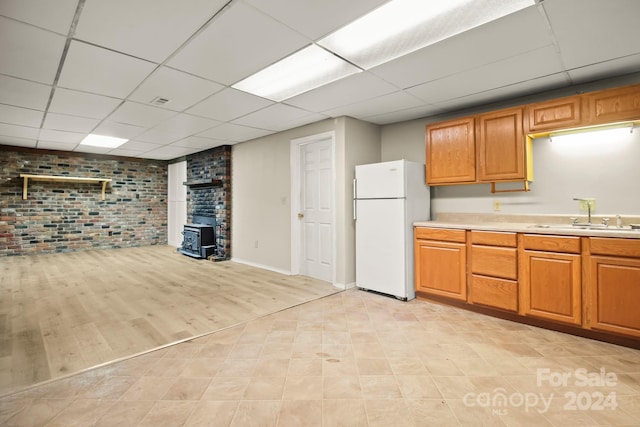 kitchen with a wood stove, sink, brick wall, white fridge, and light wood-type flooring