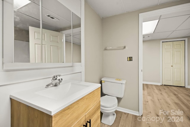 bathroom featuring wood-type flooring, vanity, toilet, and a drop ceiling