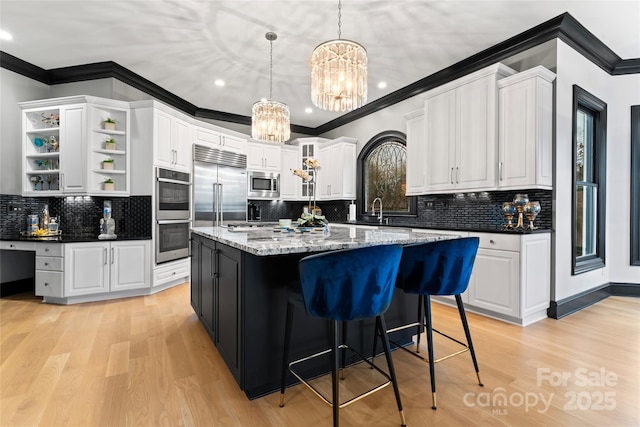 kitchen featuring built in appliances, decorative light fixtures, a center island, and white cabinets