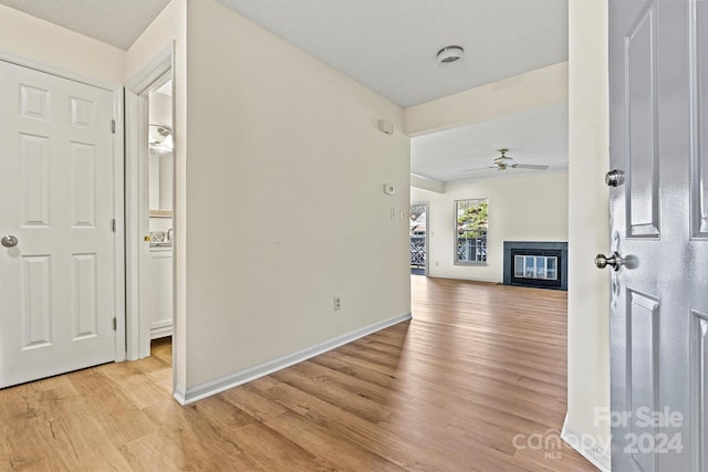 interior space with ceiling fan, a multi sided fireplace, and light wood-type flooring