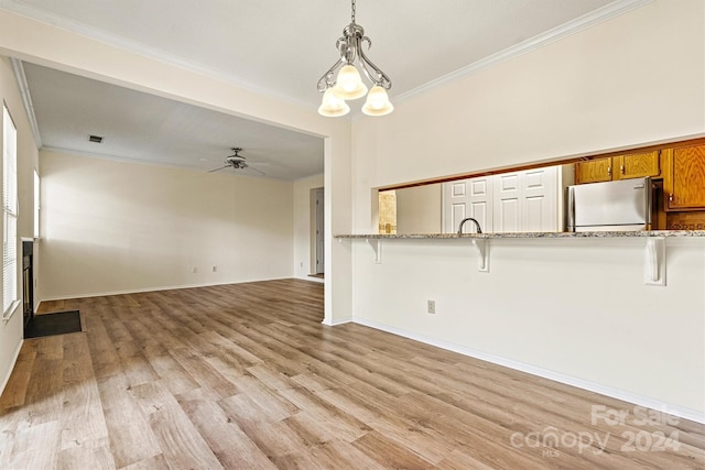 unfurnished living room featuring ceiling fan with notable chandelier, light wood-type flooring, and ornamental molding