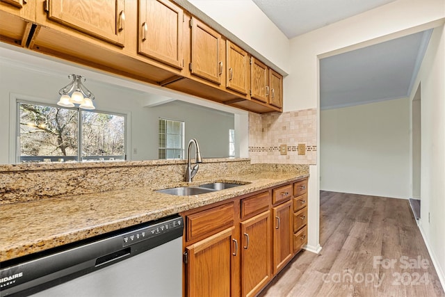 kitchen with light stone countertops, light wood-type flooring, tasteful backsplash, sink, and dishwasher