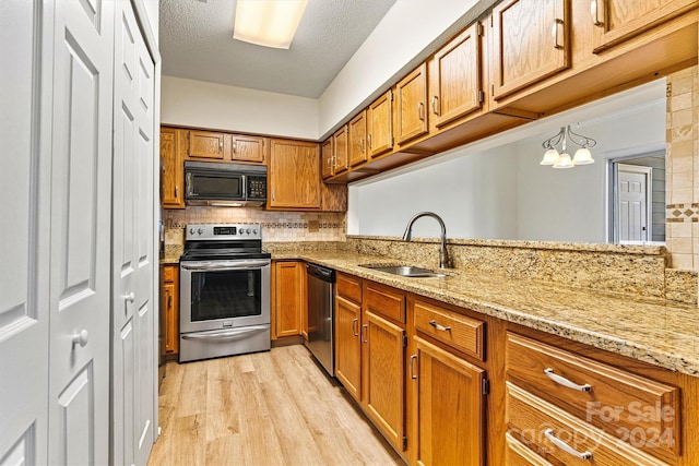 kitchen featuring light stone countertops, appliances with stainless steel finishes, backsplash, sink, and light hardwood / wood-style floors