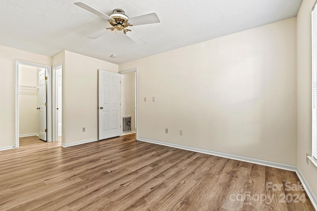 unfurnished bedroom with ceiling fan, light hardwood / wood-style floors, a walk in closet, and a textured ceiling