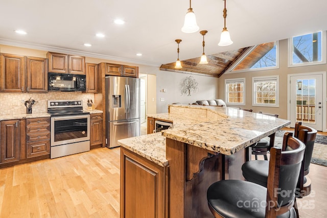 kitchen featuring pendant lighting, a breakfast bar, light stone countertops, appliances with stainless steel finishes, and a kitchen island