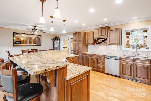 kitchen featuring sink, stainless steel dishwasher, ceiling fan, a kitchen island, and a kitchen bar