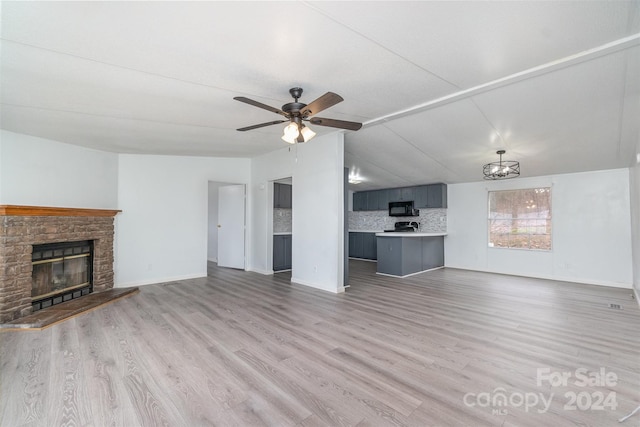 unfurnished living room featuring light wood-type flooring, a stone fireplace, ceiling fan, and lofted ceiling