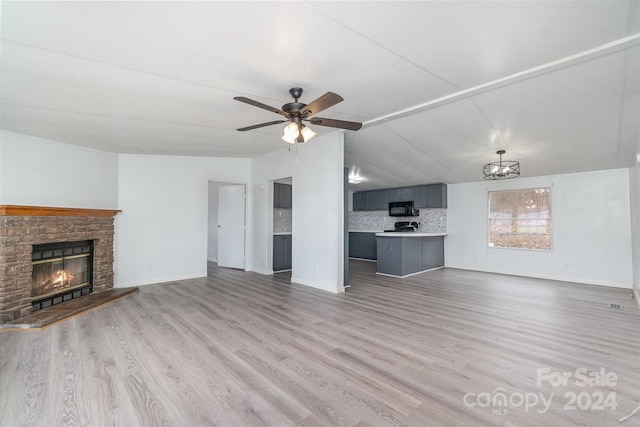 unfurnished living room featuring ceiling fan, light hardwood / wood-style floors, a stone fireplace, and vaulted ceiling