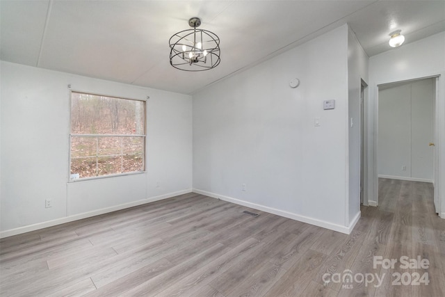 spare room featuring a chandelier and light hardwood / wood-style floors