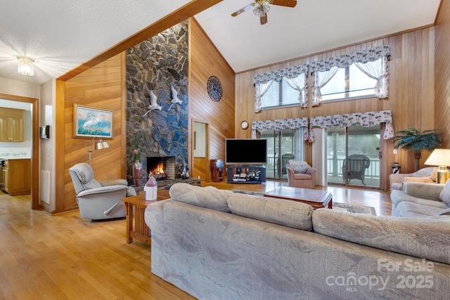 living room with high vaulted ceiling, light wood-type flooring, a fireplace, and wood walls