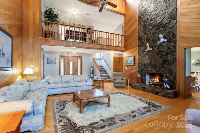 living room with wood-type flooring, a stone fireplace, and a high ceiling