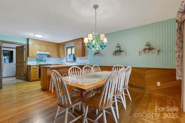 dining area featuring a notable chandelier, light hardwood / wood-style floors, a textured ceiling, and wood walls