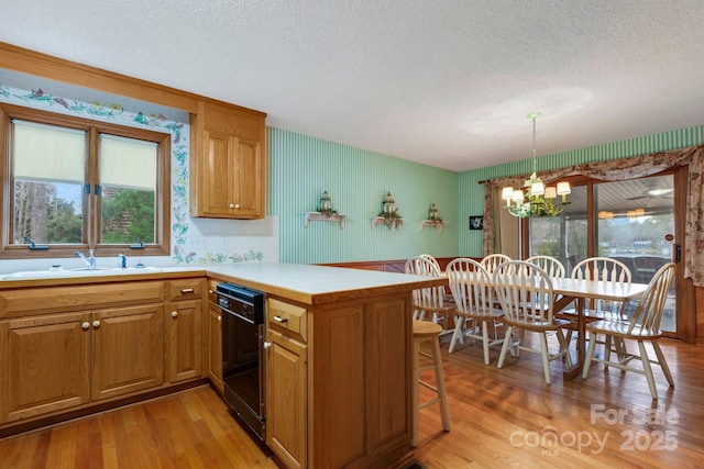 kitchen with sink, light hardwood / wood-style flooring, hanging light fixtures, black dishwasher, and kitchen peninsula