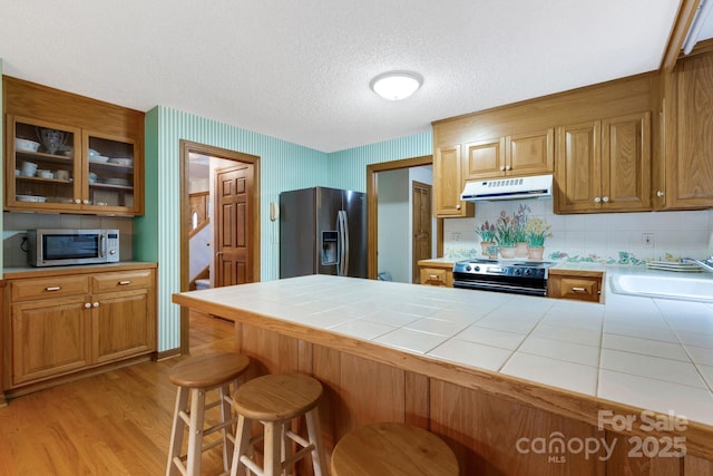 kitchen with a breakfast bar, sink, tile counters, stainless steel appliances, and light wood-type flooring