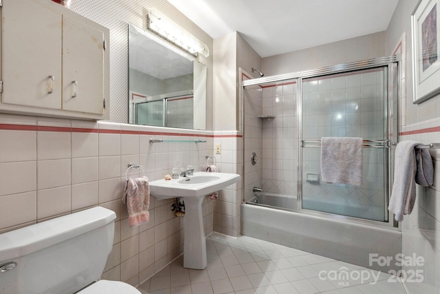 bathroom featuring tile walls, tile patterned floors, shower / bath combination with glass door, and toilet