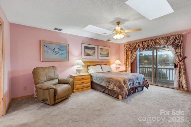 carpeted bedroom with a textured ceiling, access to exterior, ceiling fan, and a skylight