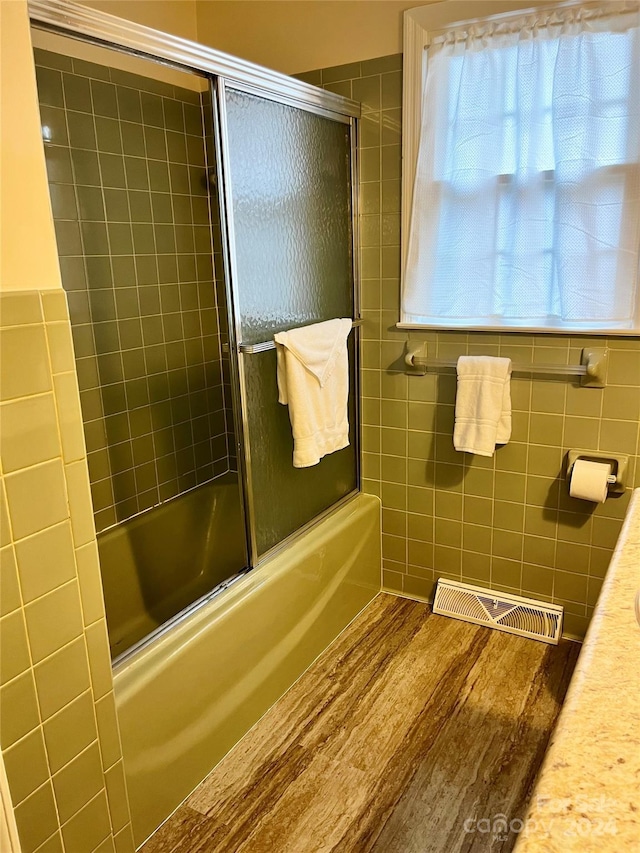 bathroom featuring hardwood / wood-style floors, enclosed tub / shower combo, and tile walls