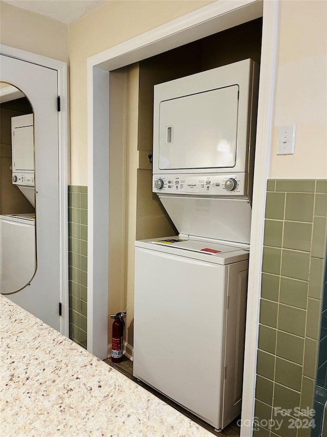 washroom with stacked washing maching and dryer and tile walls