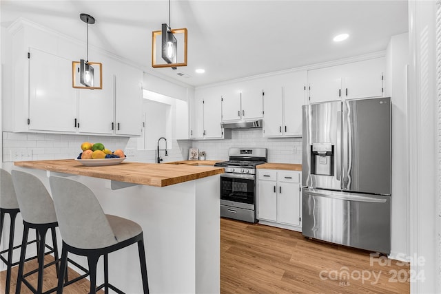 kitchen featuring a kitchen bar, stainless steel appliances, butcher block countertops, white cabinetry, and hanging light fixtures