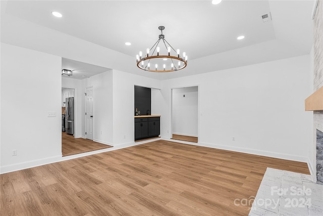 unfurnished living room featuring a chandelier, sink, and light hardwood / wood-style floors