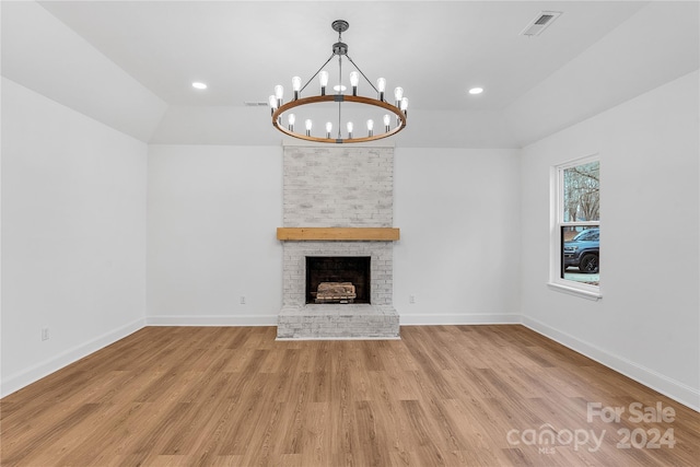 unfurnished living room with a brick fireplace, a notable chandelier, and light wood-type flooring