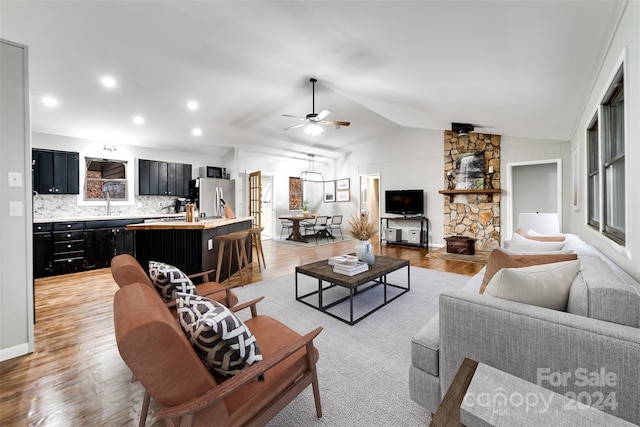 living room featuring light wood-type flooring, vaulted ceiling, ceiling fan, sink, and a fireplace