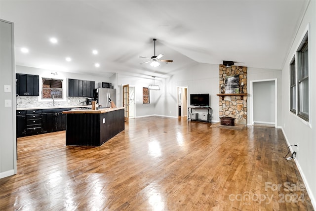 kitchen featuring a kitchen island with sink, ceiling fan, a fireplace, stainless steel fridge with ice dispenser, and lofted ceiling