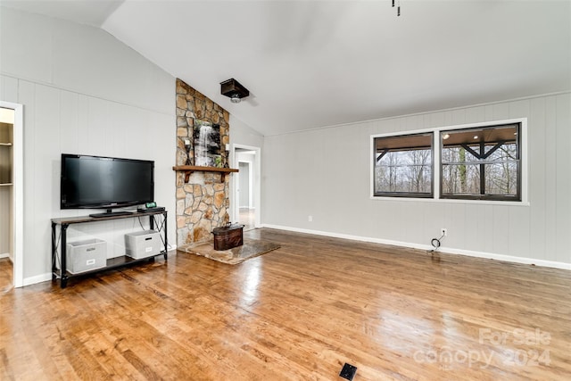 unfurnished living room featuring hardwood / wood-style floors, vaulted ceiling, and a stone fireplace