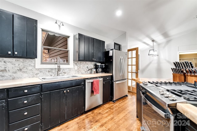 kitchen with sink, light wood-type flooring, tasteful backsplash, decorative light fixtures, and stainless steel appliances