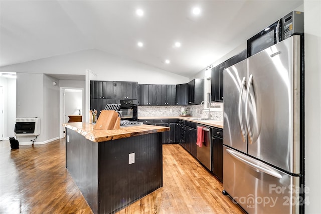 kitchen with backsplash, heating unit, vaulted ceiling, a kitchen island, and appliances with stainless steel finishes