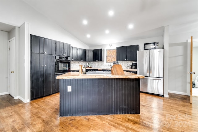 kitchen with tasteful backsplash, stainless steel fridge, oven, and a kitchen island with sink