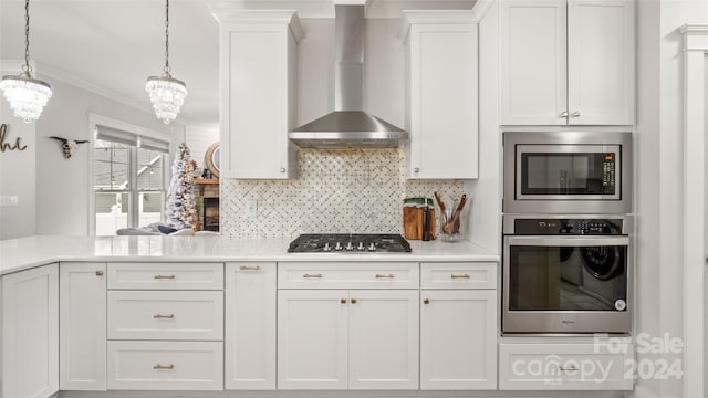 kitchen with an inviting chandelier, wall chimney range hood, hanging light fixtures, white cabinetry, and stainless steel appliances