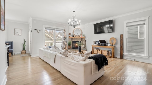 living room featuring a fireplace, light hardwood / wood-style floors, ornamental molding, and a notable chandelier