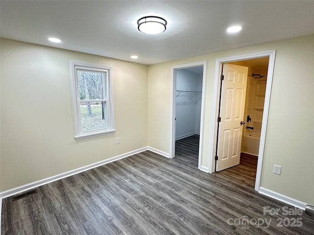 unfurnished bedroom with a walk in closet, a closet, and dark wood-type flooring