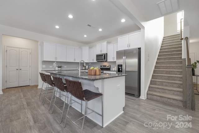 kitchen with light wood-type flooring, stainless steel appliances, a center island with sink, white cabinetry, and a breakfast bar area