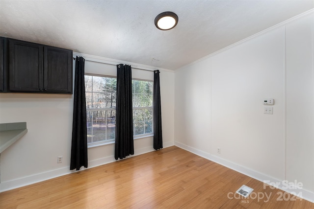 unfurnished room featuring a textured ceiling, light wood-type flooring, and crown molding