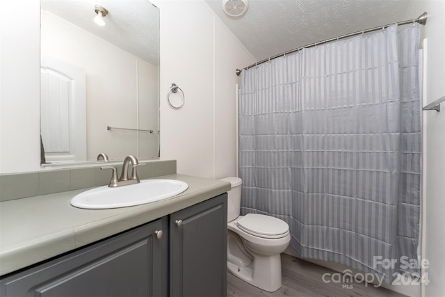 bathroom with a shower with shower curtain, vanity, a textured ceiling, wood-type flooring, and toilet