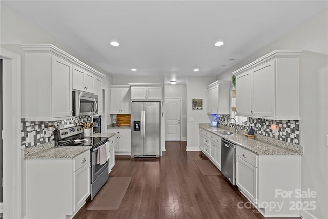 kitchen with dark wood-type flooring, white cabinets, sink, appliances with stainless steel finishes, and light stone counters