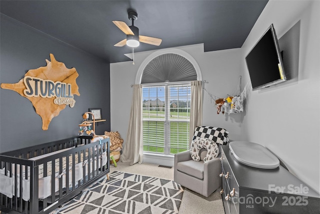 carpeted bedroom featuring ceiling fan and a crib