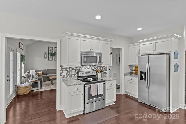 kitchen featuring dark wood-type flooring, light stone counters, backsplash, white cabinets, and appliances with stainless steel finishes