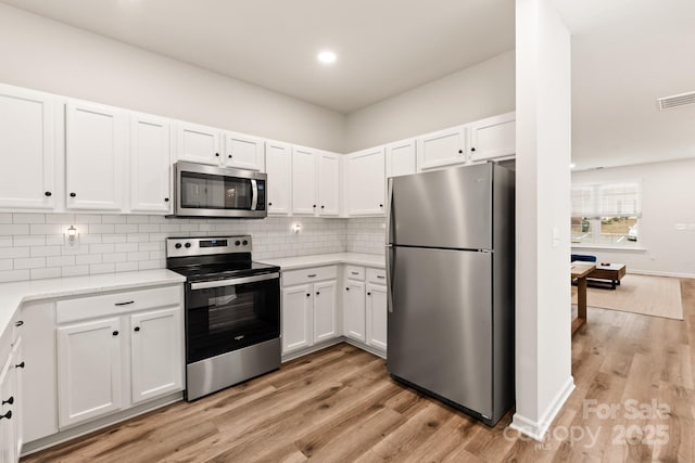 kitchen with appliances with stainless steel finishes, light hardwood / wood-style floors, white cabinetry, and tasteful backsplash