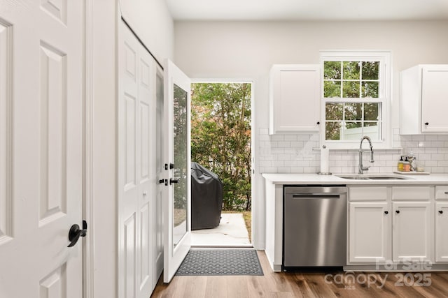 kitchen featuring decorative backsplash, stainless steel dishwasher, sink, light hardwood / wood-style flooring, and white cabinets