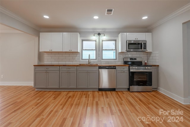 kitchen with gray cabinetry, crown molding, sink, light hardwood / wood-style flooring, and appliances with stainless steel finishes