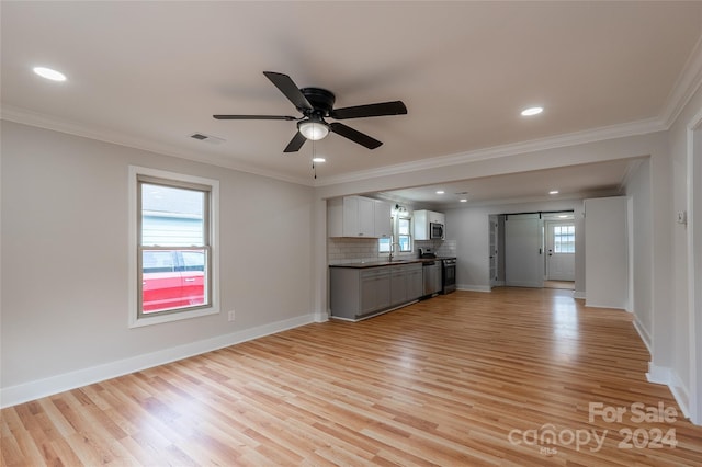 unfurnished living room with ceiling fan, sink, a barn door, light hardwood / wood-style flooring, and ornamental molding