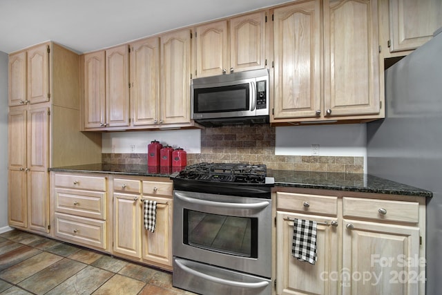 kitchen featuring dark stone countertops, light brown cabinetry, appliances with stainless steel finishes, and tasteful backsplash