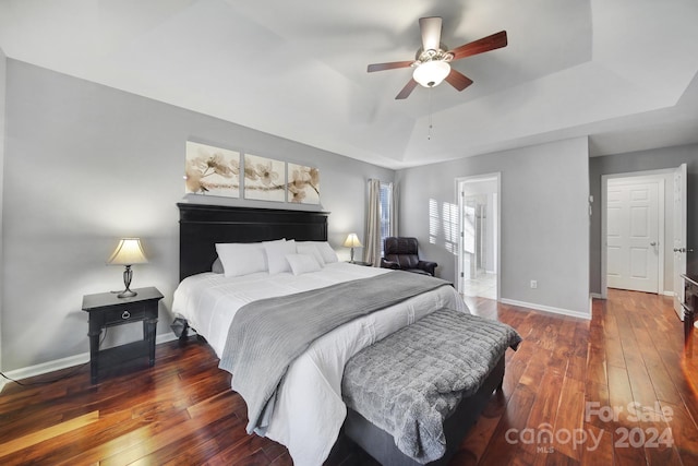 bedroom with ceiling fan, dark wood-type flooring, and a tray ceiling