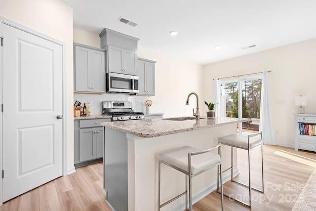 kitchen featuring sink, a kitchen bar, a kitchen island with sink, light stone counters, and stainless steel appliances