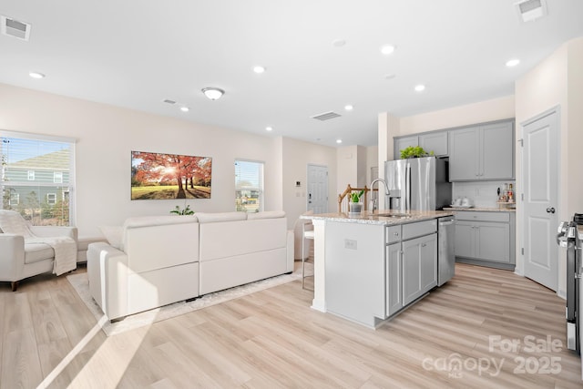 kitchen featuring appliances with stainless steel finishes, sink, gray cabinets, and a kitchen island with sink