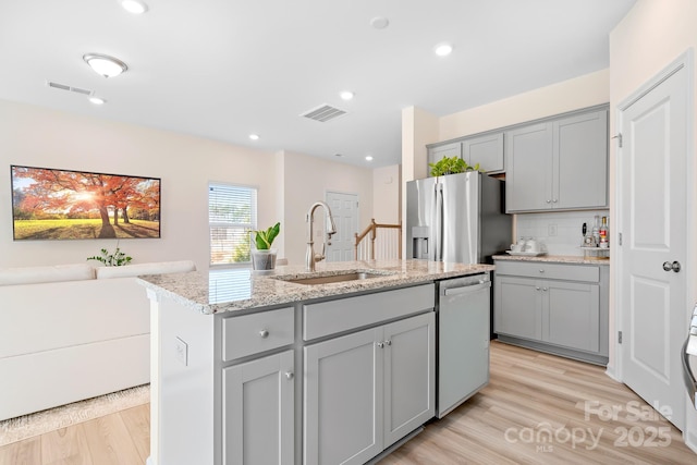 kitchen with sink, gray cabinetry, stainless steel appliances, light stone counters, and an island with sink