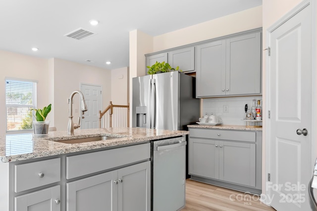 kitchen with light stone counters, sink, gray cabinetry, and appliances with stainless steel finishes